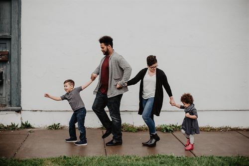 A young boy and a young girl hold hands and walk with their mom and dad.